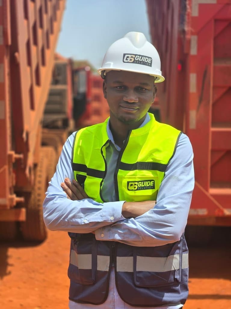 Responsable en casque blanc et gilet Guide Solution, bras croisés, devant des camions-bennes
